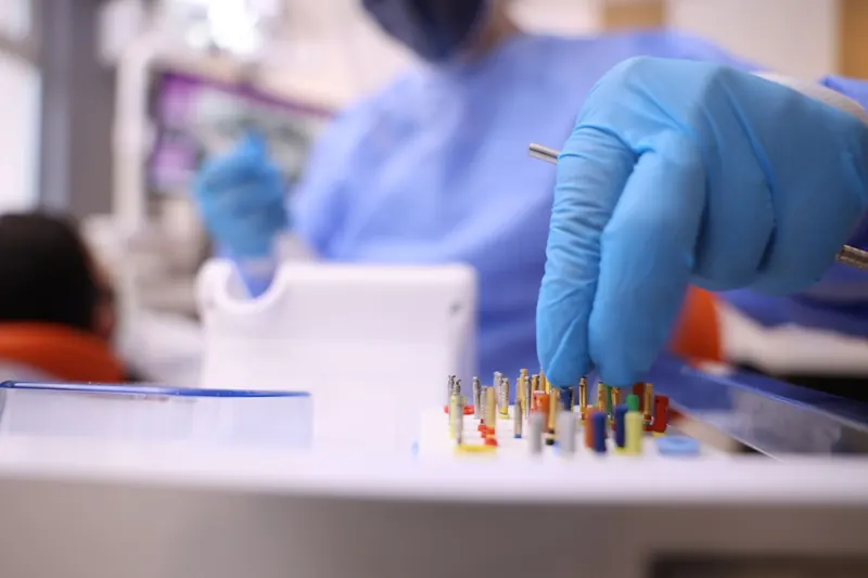 Mão de luva azul separando instrumentos odontológicos